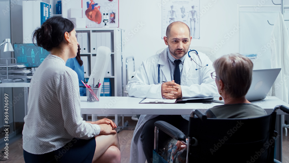 Doctor giving a consultation for elderly disabled woman with her daughter in medical office. Dsabled disability handicapped old person treatment in modern private hospital or clinic. Medicine and