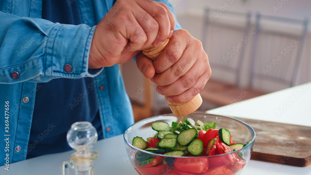 Man pouring salt over healthy salad in kitchen for delicious meal. Cooking preparing healthy organic food happy together lifestyle. Cheerful meal in family with vegetables Man pouring salt over healthy salad in kitchen for delicious meal. Cooking preparing healthy organic food happy together lifestyle. Cheerful meal in family with vegetables