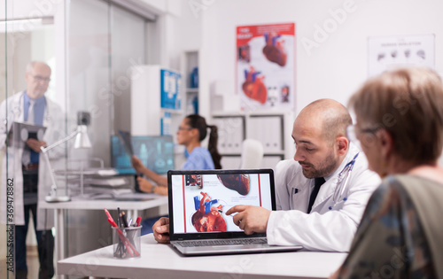 Wall Mural Young doctor pointing at heart on laptop screen in hospital office