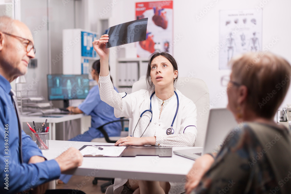 Worried doctor examining x-ray of senior patient in hospital office. Pensioner couple during medical consultation. Medic wearing white coat and stethoscope. Worried doctor examining x-ray of senior patient in hospital office. Pensioner couple during medical consultation. Medic wearing white coat and stethoscope.