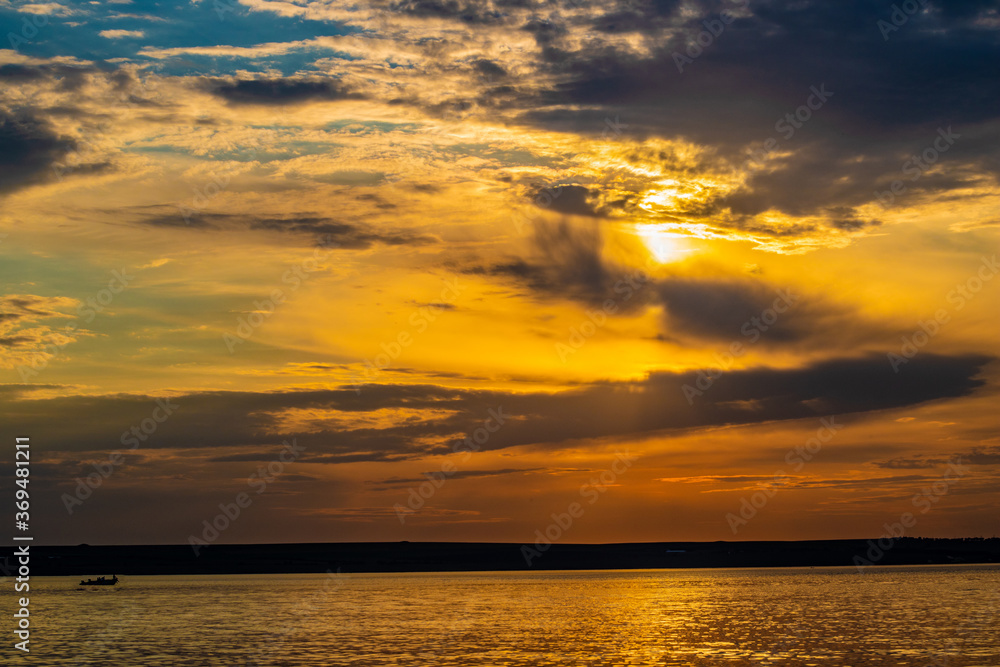 Fototapeta premium Sunset through the clouds over the water and ship on the water