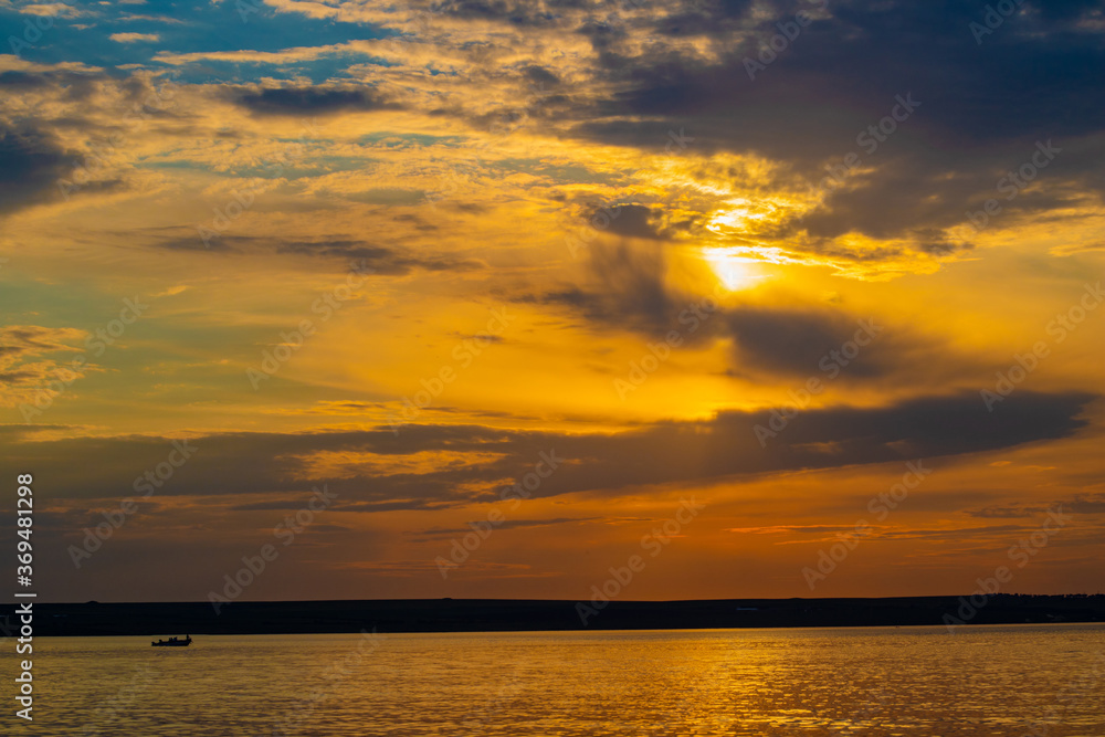 Obraz premium Sunset through the clouds over the water and ship on the water