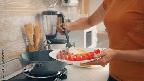Housewife cooking eggs for breakfast in kitchen. Healthy morning with fresh products, happy lifestyle for housewife who is cooking in cozy modern kitchen under warm sunny summer morning light