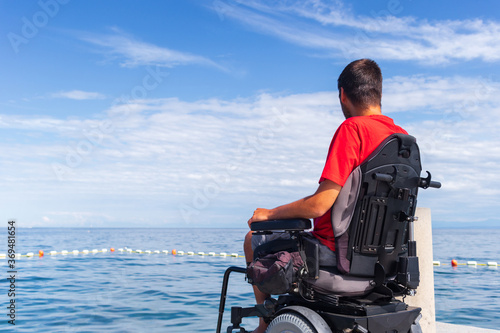 Man sitting in a wheelchair on the beach. Dangers of jumping into water from heights. Head and spine injury. © 24K-Production
