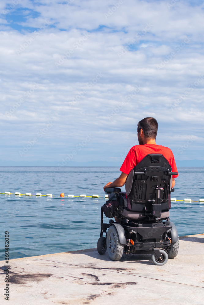 Man sitting in a wheelchair on the beach. Dangers of jumping into water