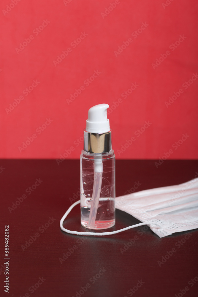 Spray bottle with antiseptic. For treating hands from viruses. A medical mask lies nearby. On a coral background. Spray bottle with antiseptic. For treating hands from viruses. A medical mask lies nearby. On a coral background.