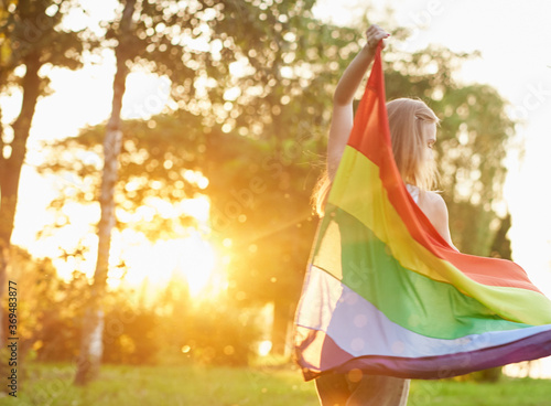 Woman dancing with rainbow lgbt flag behind back.
