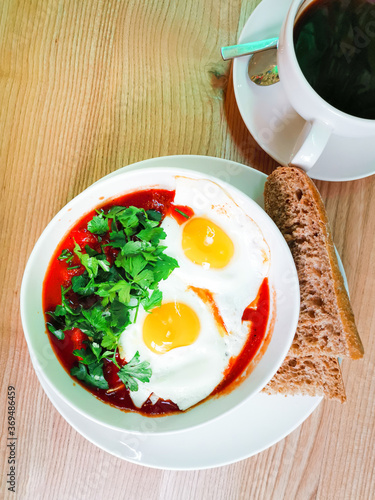 Two fried eggs cooked with tomato sauce and vegetables served with two pieces of homemade bread in white plate for an healthy breakfast