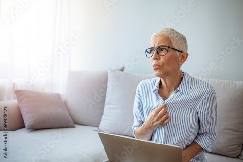 Mature Woman Experiencing Hot Flush From Menopause. Tired mature woman tolerating hot flash. Hot flashes. Exhausted mature woman resting on sofa and having hot flash photo