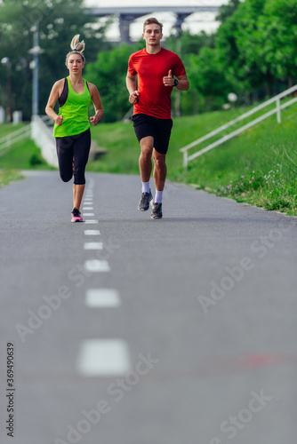 Young running couple jogging on an asphalt road in the park © qunica.com