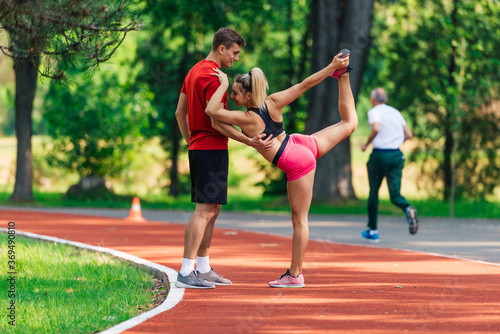 Young male athlete supporting his young female partner while she is stretching her legs after running on a race track.