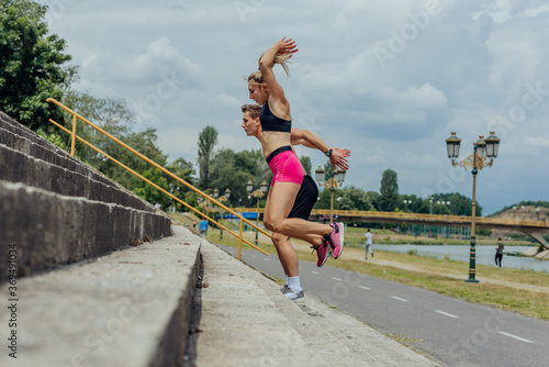 Side view picture of  active sporty couple jumping up on stairs in a park