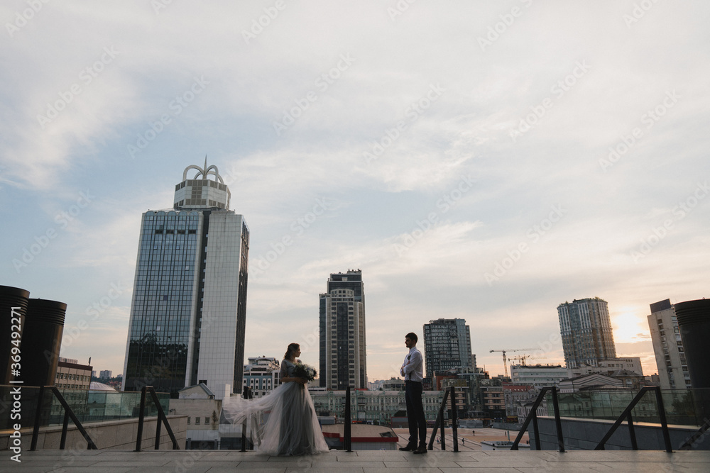 Fototapeta premium Romantic and happy caucasian couple in wedding clothes walking and hugging at the city streets. Love, relationships, romance, happiness, urban concept. Bride and groom celebrate their marriage.