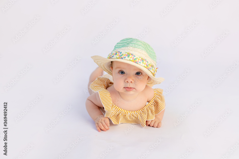 smiling baby girl 6 months old in a swimsuit and sun hat lying on a white isolated background, space for text smiling baby girl 6 months old in a swimsuit and sun hat lying on a white isolated background, space for text