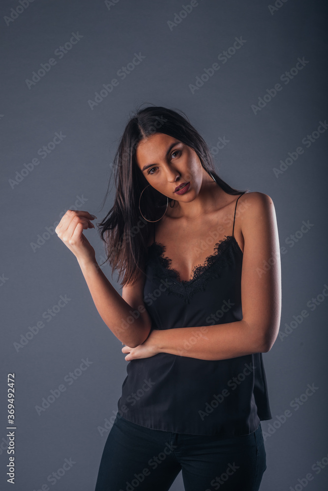 Sensual studio portrait of a sexy woman standing with one arm crossed on a gray background