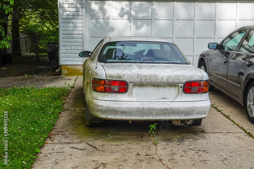 Fototapeta Rear view of an extremely dirty white car in a driveway in front of a white gara