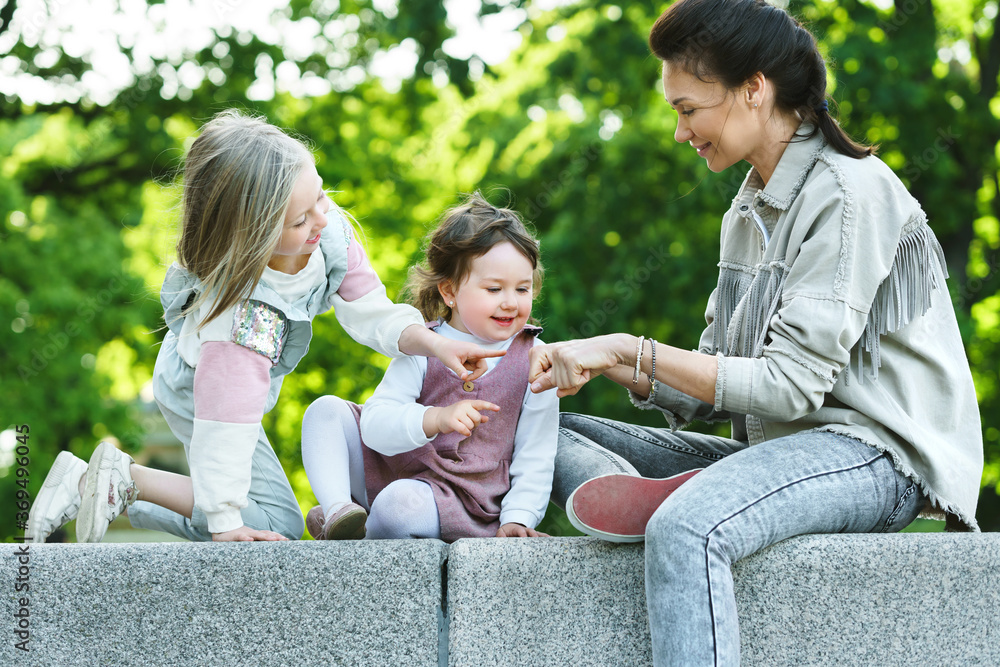 Happy mother and her two daughters sitting and playing in a city park