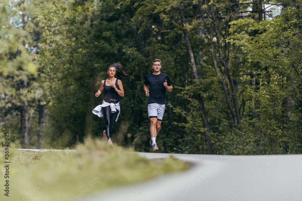 Obraz premium Young fit couple atheltes running on running road in a forest.