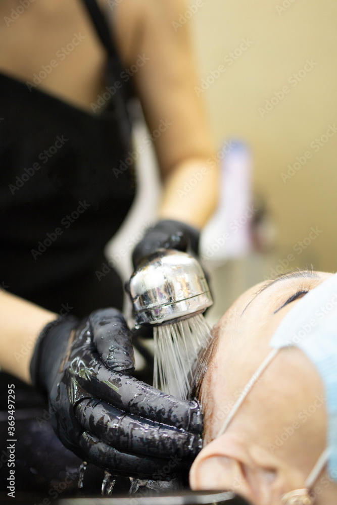 Hairdressing services during the coronavirus. Hands of hairdresser washing head of woman in mask. Hairdresser washing head of woman
