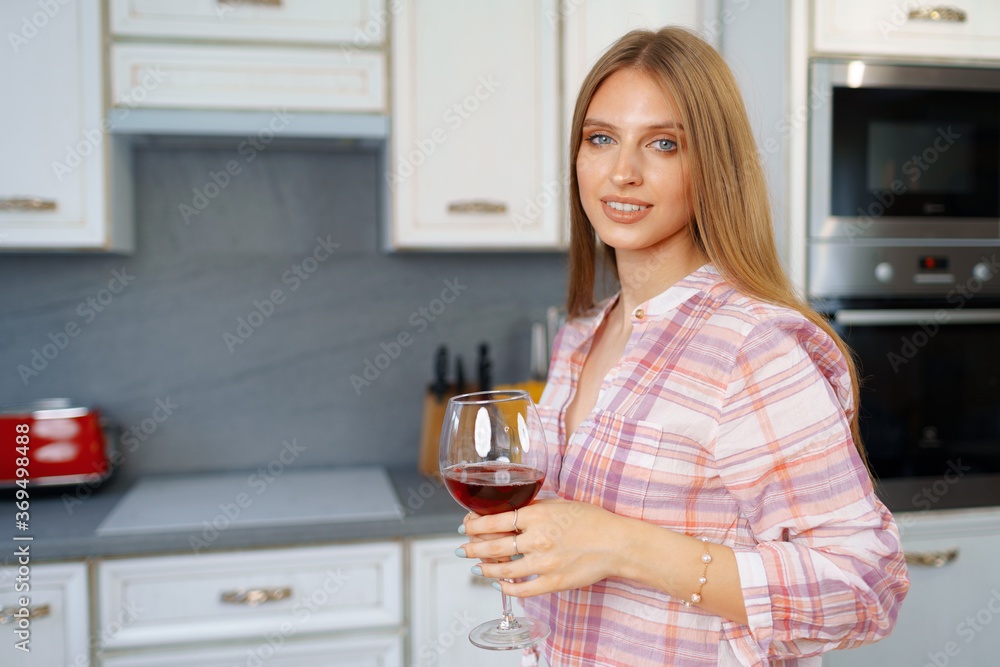 Blonde caucasian woman with glass of red wine standing in her kitchen Blonde caucasian woman with glass of red wine standing in her kitchen