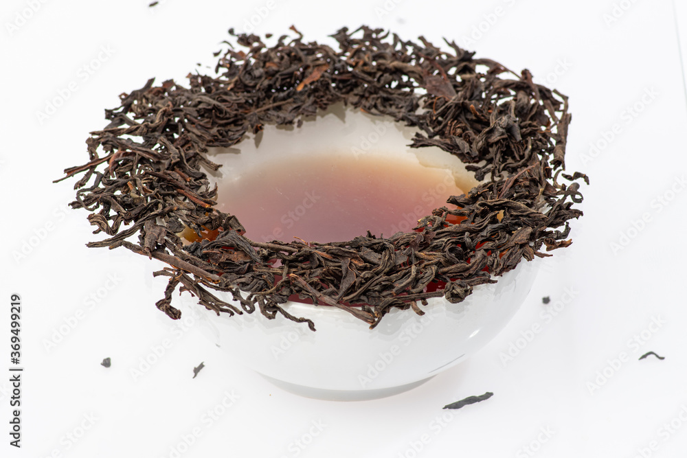 loose black tea next to a cup of tea on a white background loose black tea next to a cup of tea on a white background