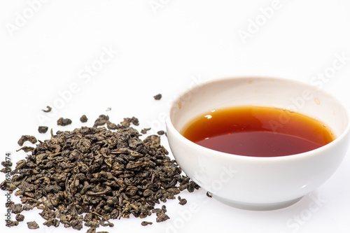 loose black tea next to a cup of tea on a white background
