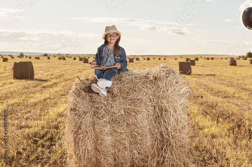 Reading girl sits over the haystack roll on field in countryside. High quality photo