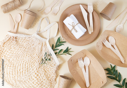 Zero waste, plastic-free and eco-friendly living. Paper disposable tableware, wooden cutlery and cotton mesh bag top view on beige table