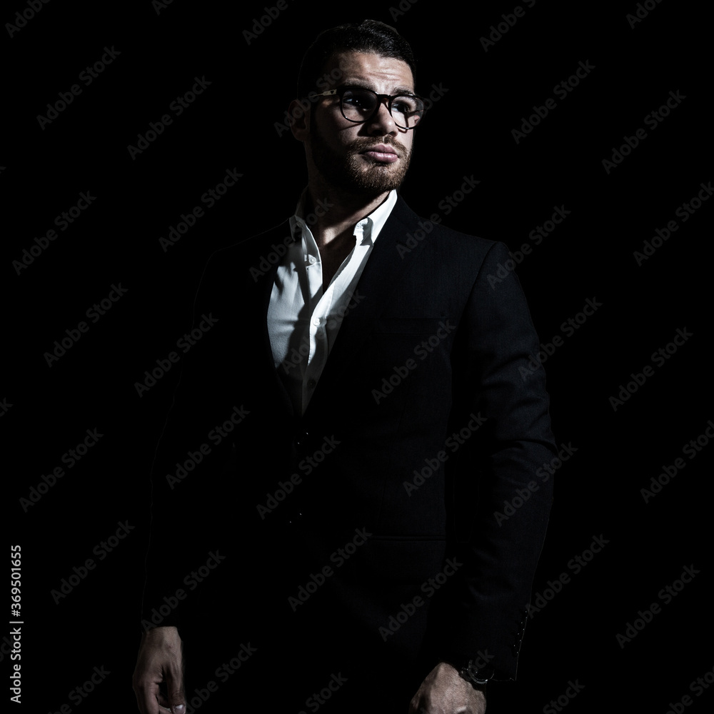 Business portrait of a young caucasian man in a black classic suit on a black background. 