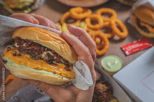 Point of view of a person eating a handmade burger, with several portions of fried snacks on the table