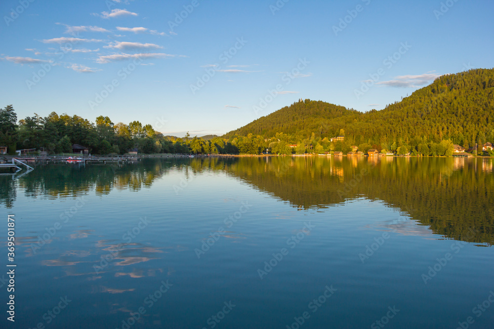 A view of a mountain alpine lake on a evening. Lake with hills, water and blue sky with clouds. Green forest by the lake in reflection in the water beauty in nature