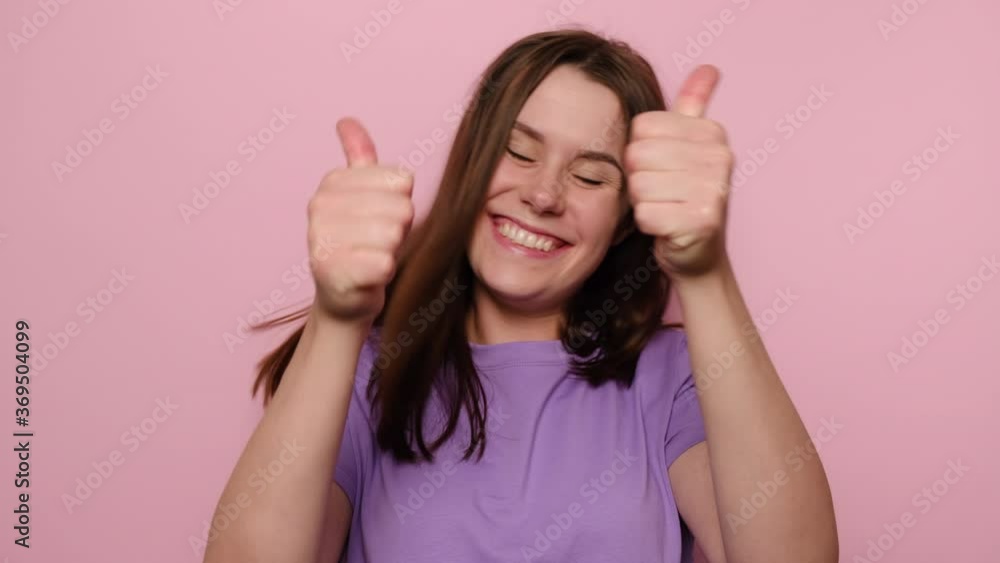 Excited young woman winking and vigorously showing double thumbs up, like gesture, demonstrating approval, feeling enthusiastic satisfied with excellent result, isolated on pink studio background Excited young woman winking and vigorously showing double thumbs up, like gesture, demonstrating approval, feeling enthusiastic satisfied with excellent result, isolated on pink studio background