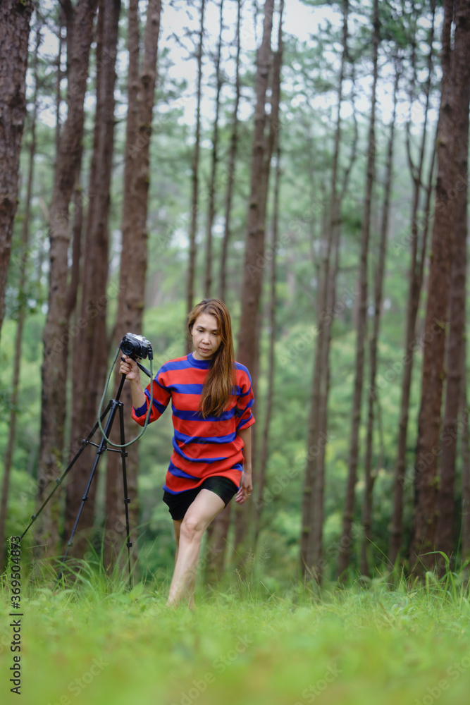 An Asian woman in a red dress holding a camera with a pine forest in the background An Asian woman in a red dress holding a camera with a pine forest in the background