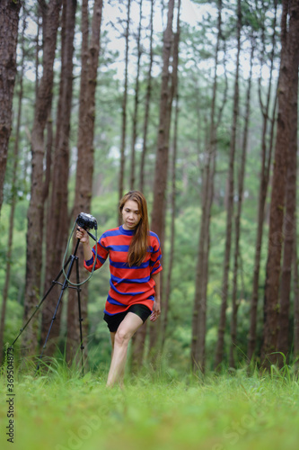 An Asian woman in a red dress holding a camera with a pine forest in the background