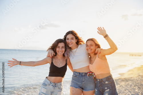 Portrait of three young female friends having fun on the sea shore looking at camera laughing. 