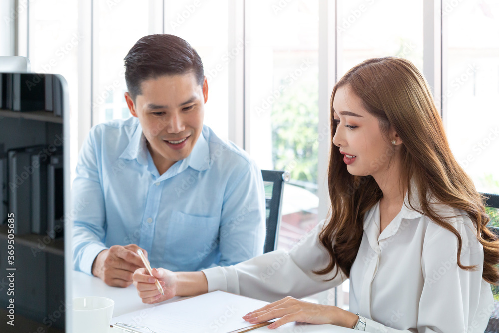 Fototapeta premium Businessman and businesswoman sitting working together at modern office. Couple working together talking and discussing at small office. Happy business colleagues in modern office helping each other.