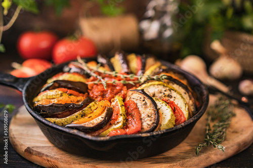 Ratatouille made of zucchini  eggplants  peppers  onions  garlic and tomatoes slices with aromatic herbs  bread. Rustic wooden table. Traditional French food  vegetable  vegan healthy dish. Copy space