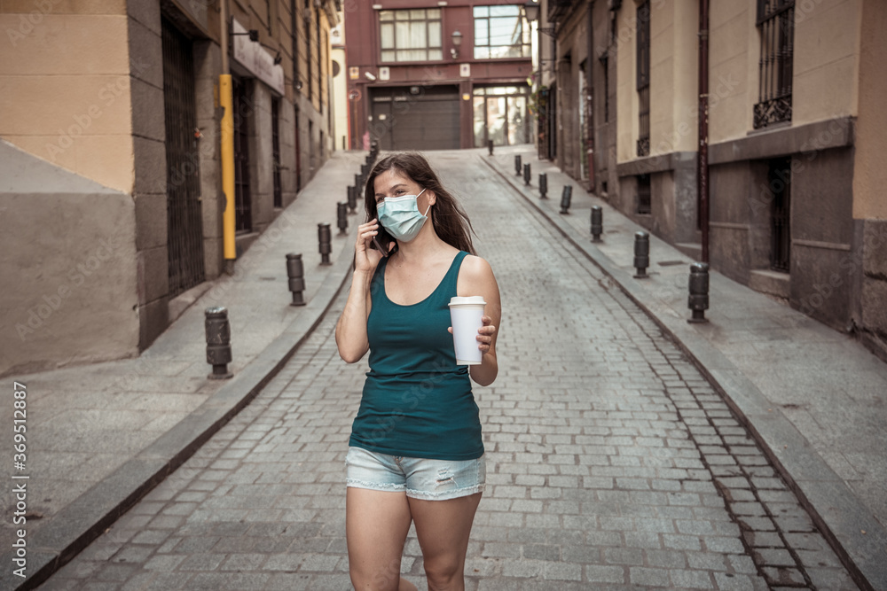 Woman wearing surgical protective face mask talking on mobile phone in public space in the city Woman wearing surgical protective face mask talking on mobile phone in public space in the city