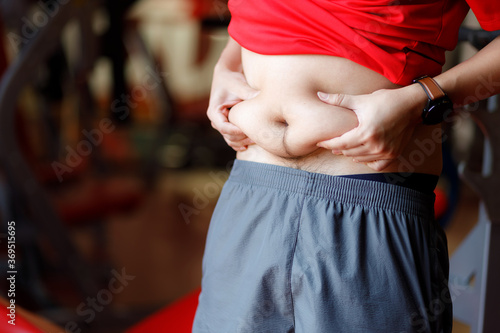 Fat man, Obese man hand holding excessive belly fat isolated on gym background.