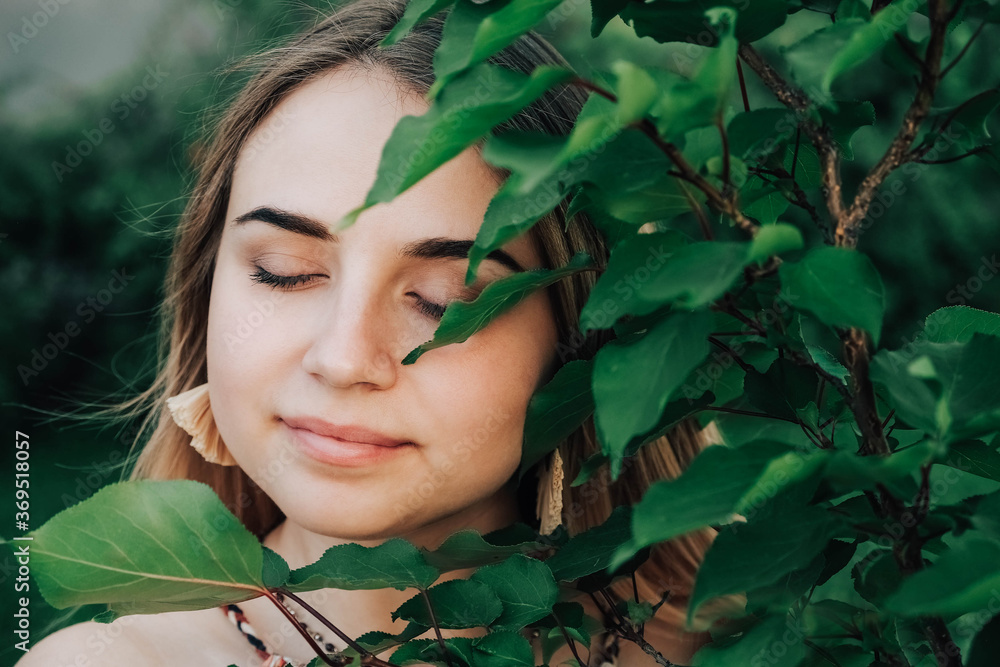 Portrait of a beautiful blonde girl with closed eyes in a green leaves trees. Copy, empty space for text. Copy, empty space for text Portrait of a beautiful blonde girl with closed eyes in a green leaves trees. Copy, empty space for text. Copy, empty space for text