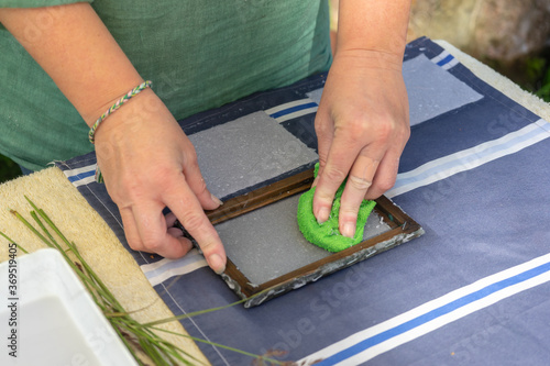 Woman holding frame for making paper sheets from waste paper pulp. Selective focus. Decorative and applied art. Recycling concept, ecology.