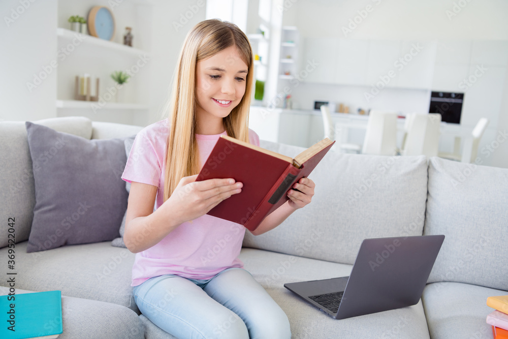 Photo of positive girl kid sit divan study remote read text book prepare homework for tomorrow homeschool lesson wear t-shirt denim jeans in modern apartment house indoors Photo of positive girl kid sit divan study remote read text book prepare homework for tomorrow homeschool lesson wear t-shirt denim jeans in modern apartment house indoors