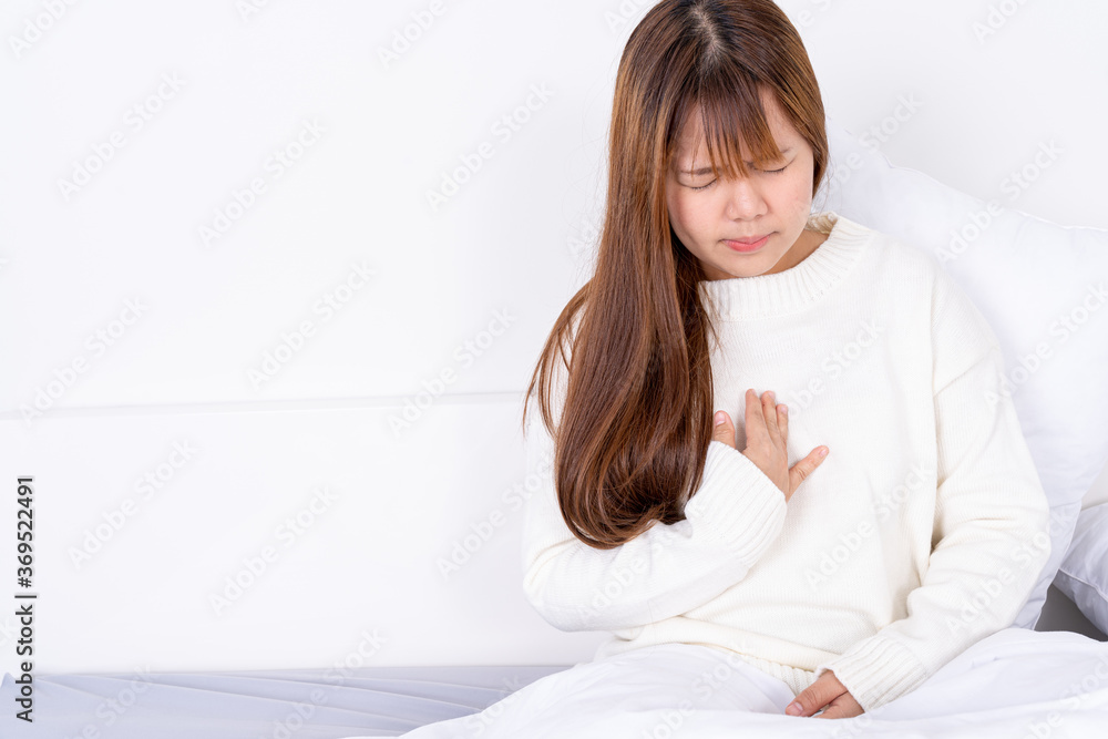 Young woman suffering from chest pain after wake up on the bed. Healthcare medical or daily life concept. Young woman suffering from chest pain after wake up on the bed. Healthcare medical or daily life concept.