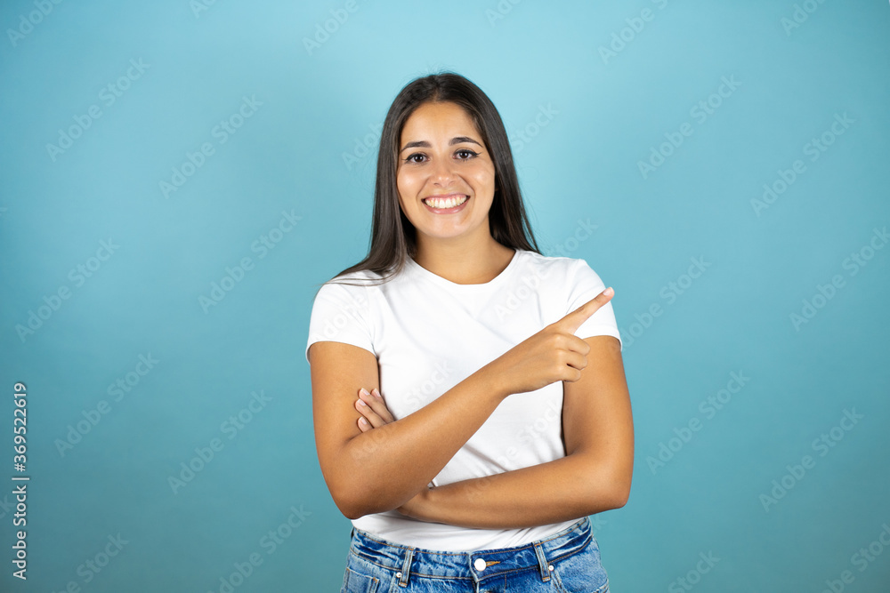 Young beautiful woman standing over isolated blue background smiling happy pointing with hand and finger to the side Young beautiful woman standing over isolated blue background smiling happy pointing with hand and finger to the side