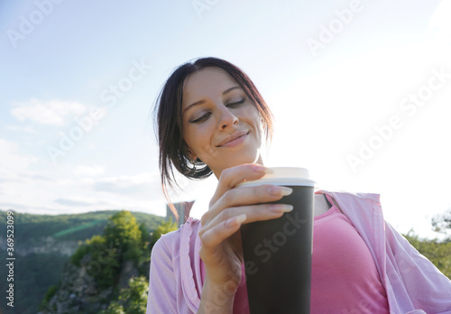 Young woman holding cup of coffee in hand with blue sky and mountains in the background photo