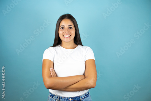 Young beautiful woman standing over blue isolated background smiling with her arms crossed © Irene