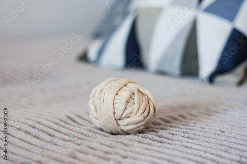 a ball of white acrylic yarn for knitting on a gray bedspread with decorative pillows, a cozy home interior.