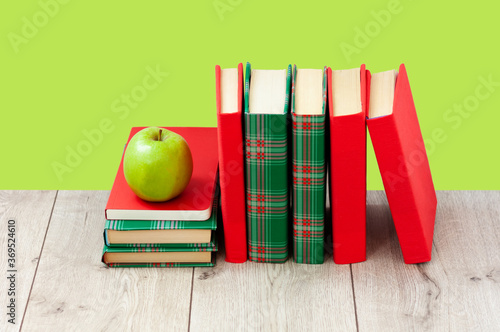 Back to school, pile of books in colorful covers and green apple on wooden table with lime mint green background. Distance home education. Quarantine concept of stay home.