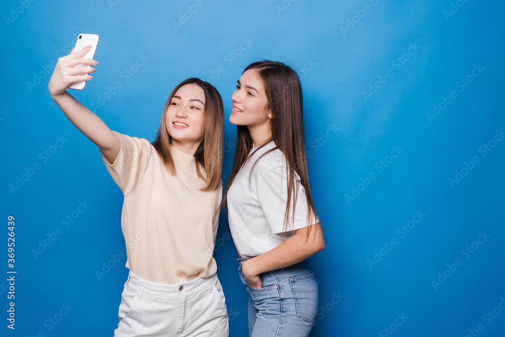 Two young women making selfie photo over blue background Two young women making selfie photo over blue background