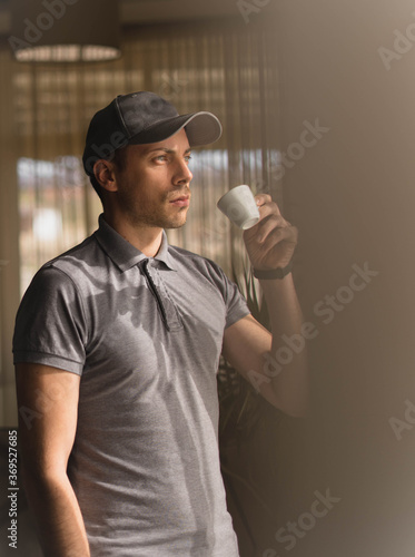 A young man drinks coffee by the window